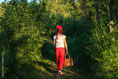 Young girl walking on a path through green woods carrying a birchbark basket