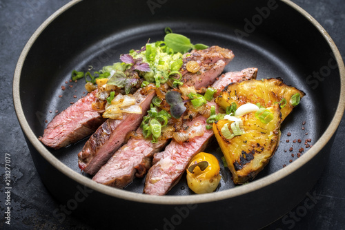Modern Barbecue dry aged wagyu flank steak with pineapples and chimichurri sauce as top view on a plate