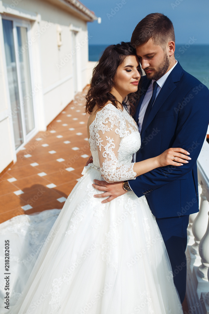 Naklejka premium Beautiful Bride and Groom enjoy each other on the background of the ocean. happy romantic young couple celebrating their marriage. Sexy stylish couple of lovers close up portrait. wedding concept.