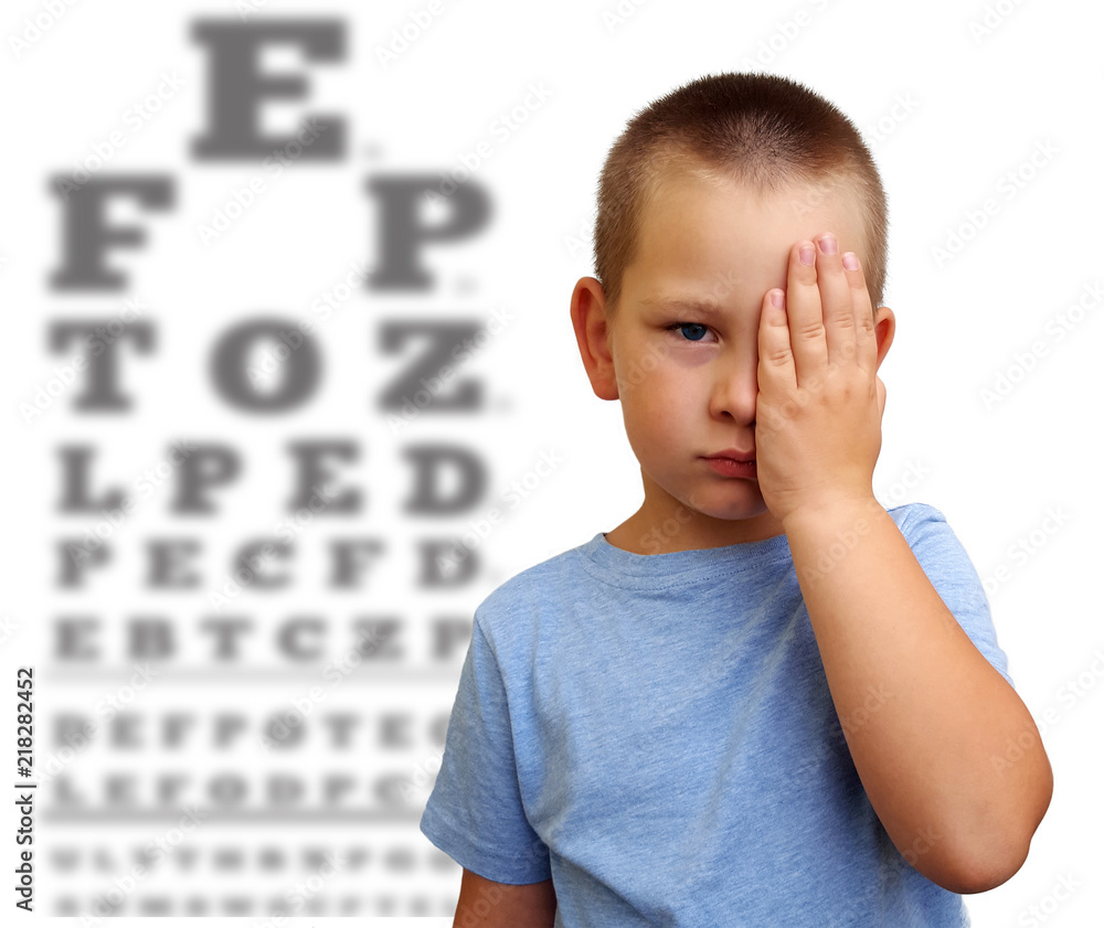 Little boy covering one eye with palm for eyesight exam with blurry eye chart behind Stock Photo