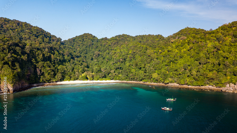 Aerial drone view of a beautiful tropical island with sandy beach and lush green vegetation surrounded by tropical coral reef