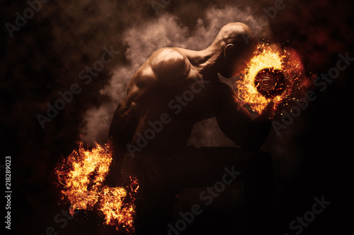 Strong young man bodybuilder performing exercise for biceps with burning dumbbell. Concept Artistic Gym Life Style.