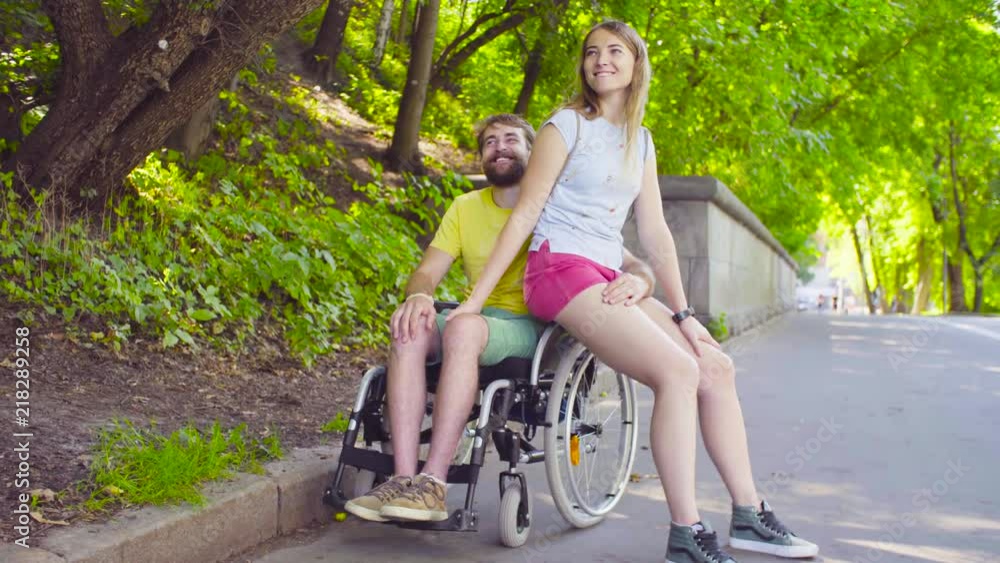 Happy young disable man in a wheelchair in the park with his wife ...