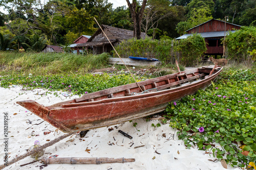 A small  traditional wooden fishing boat on the beach next to a small fishing village in Myanmar