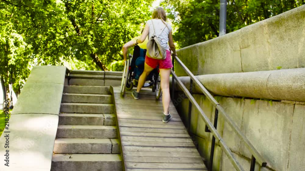 A young woman helping a disabled man in a wheelchair to ride down a ramp with a big slope A young woman helping a disabled man in a wheelchair to ride down a ramp with a big slope