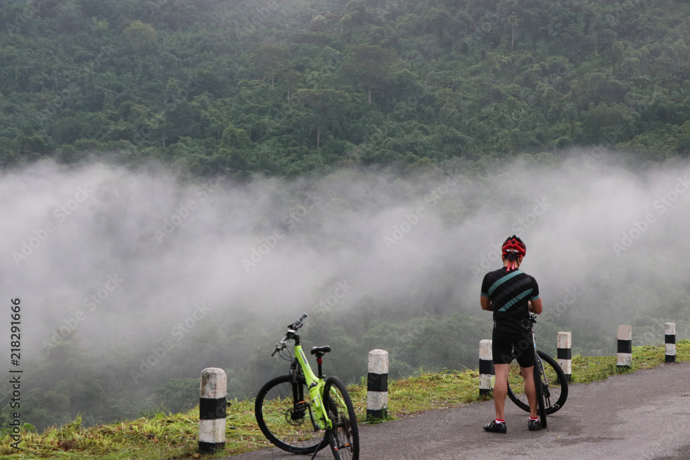 Nakorn Na Yok Province Thailand, Jul 28 2018 time 7.16 am One people stop ride bicycle because a lot of mist on the road near the mountain beautiful view and good healthy in the morning time