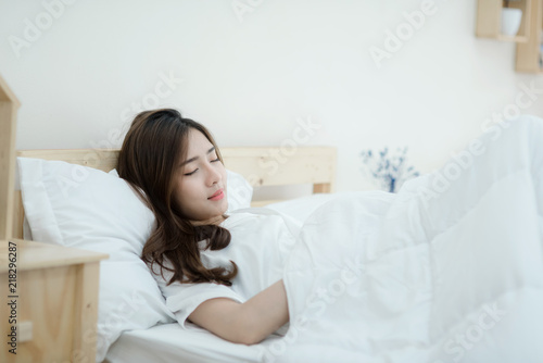 A beautiful young woman sleeping in bed. Happy morning. Portrait of a smiling pretty young lady relaxing in white bed.