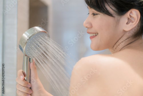 Young Asian woman taking a shower in the bathroom with Shower head. Looking happy and relax.