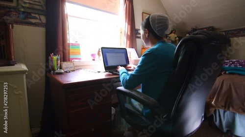 A young Mennonite woman smiling and talking as she works on a computer at her desk in slow motion.