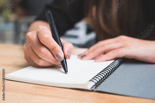 Closeup image of a woman writing down on a white blank notebook on wooden table