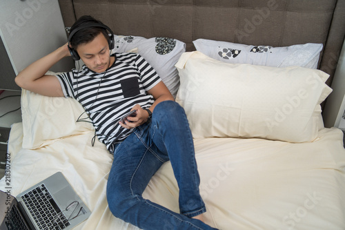 asian man using handphone and listening to music at bedroom