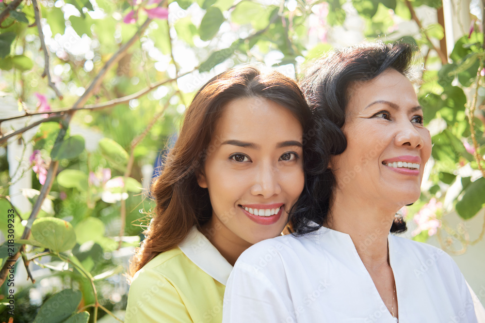 Happy beautiful young Asian woman with senior mother in summer blooming garden Happy beautiful young Asian woman with senior mother in summer blooming garden