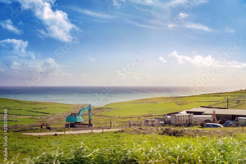 Ocean coast with a green excavator and a farm photo