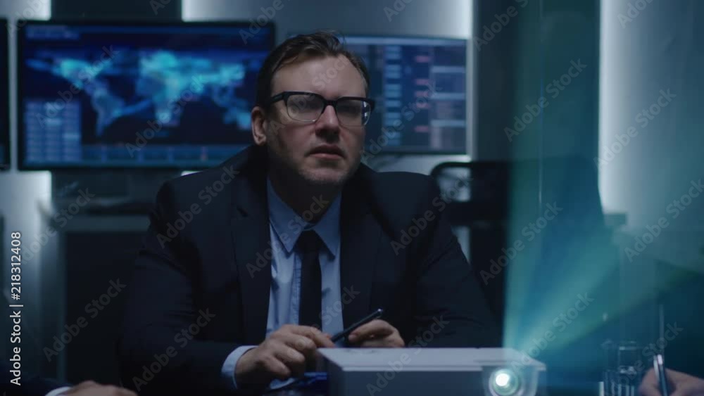 Chairman of the Board of Director Watches Presentation in the Conference Room, Making Comments to His Partners and Advisors. Working Projector on the Table Illuminates Dark Room. Chairman of the Board of Director Watches Presentation in the Conference Room, Making Comments to His Partners and Advisors. Working Projector on the Table Illuminates Dark Room.