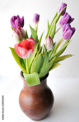 Pink and lilac tulips in a brown clay jug. On white background, isolated