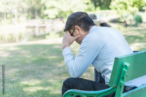 Side view of stressful businessman sitting on bench in the park. Man having a work issue worry sitting in the park.