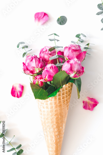 Creative minimalist composition with waffle cone with pink roses and eucalyptus inside on white background. The concept of gift and celebration. Flat lay, top view.