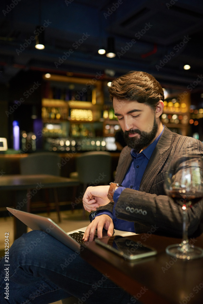 Businessman checking time when working on laptop in bar at night
