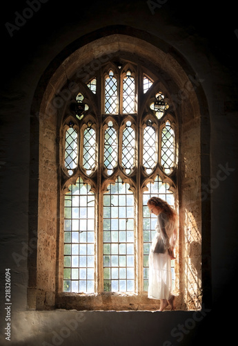 Beautiful model with long red hair posing in a Gothic window