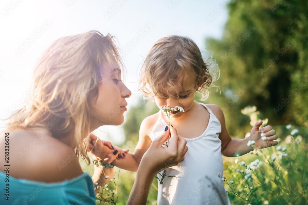 adorable daughter sniffing flowers from mom hands in field - obrazy, fototapety, plakaty 