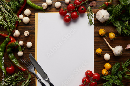 top view of blank card, cutlery and fresh herbs with vegetables on wooden surface