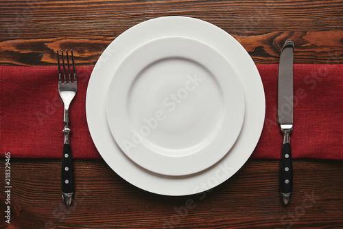 top view of round empty white plates with fork and knife on wooden table