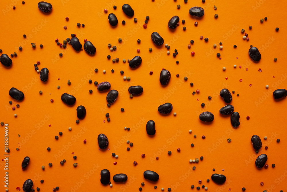 top view of haricot beans and peppercorns on orange background