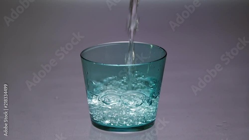 Pouring clear water into a blue glass until it overflows in slow motion.
