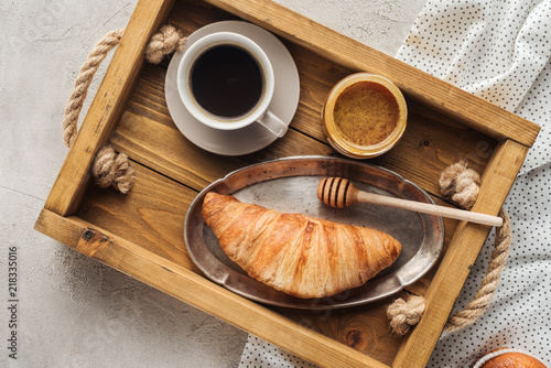 top view of cup of coffee with croissant and honey on tray on concrete surface