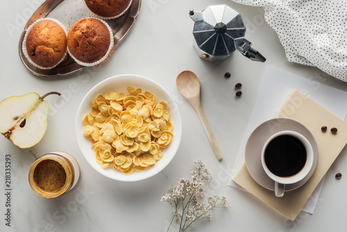 top view of bowl of dry cereal with coffee and muffins on white