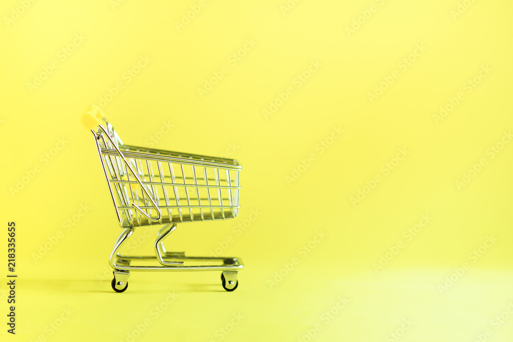 Shopping cart on yellow background. Minimalism style. Creative design. Copy space. Shop trolley at supermarket. Sale, discount, shopaholism concept. Consumer society trend