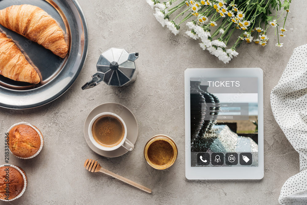 top view of coffee with pastry and tablet with tickets app on screen on concrete surface top view of coffee with pastry and tablet with tickets app on screen on concrete surface