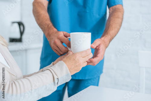 cropped shot of caregiver giving cup of hot beverage to senior woman