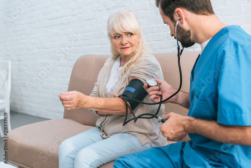 social worker measuring blood pressure to senior woman sitting on couch