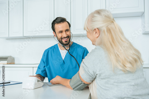 smiling male nurse measuring blood pressure to senior woman