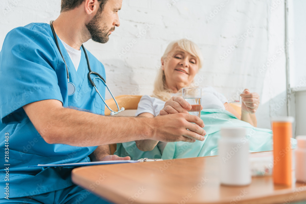 cropped shot of young doctor giving glass of water to senior woman taking medicine in bed cropped shot of young doctor giving glass of water to senior woman taking medicine in bed