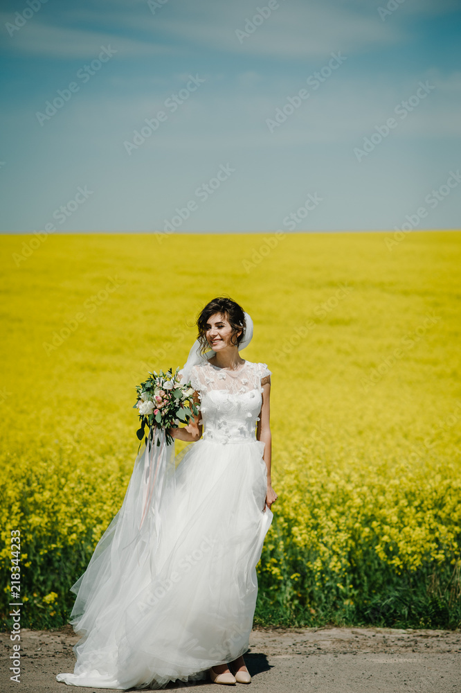 The bride with bouquet of flowers stand along the field in the nature after the wedding ceremony. The best marriage day. Portrait Girl on straight road country. The bride with bouquet of flowers stand along the field in the nature after the wedding ceremony. The best marriage day. Portrait Girl on straight road country.