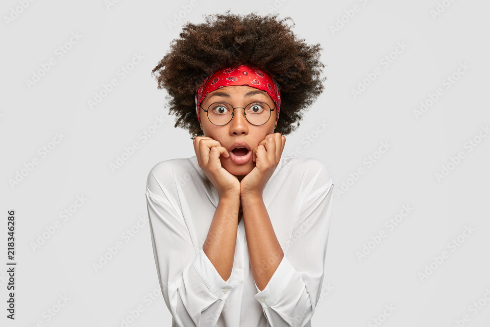 Scared dark skinned woman opens mouth from fright, keeps hands under ...