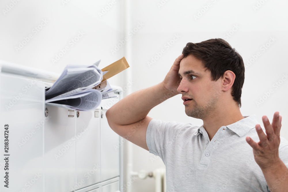 Man with hand on head in front of overloaded mailbox Man with hand on head in front of overloaded mailbox