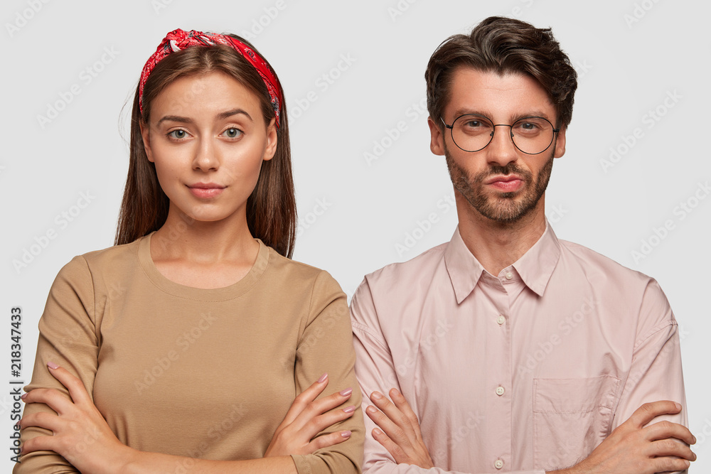 Horizontal shot of pretty European female and male students have serious confident expressions, keep hands crossed, wait for exam results, wear stylish clothing, isolated on white background Horizontal shot of pretty European female and male students have serious confident expressions, keep hands crossed, wait for exam results, wear stylish clothing, isolated on white background