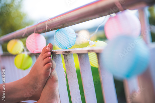 Bunte Papierlaternen an einem lauen Sommerabend, Frauenfüße an Veranda photo