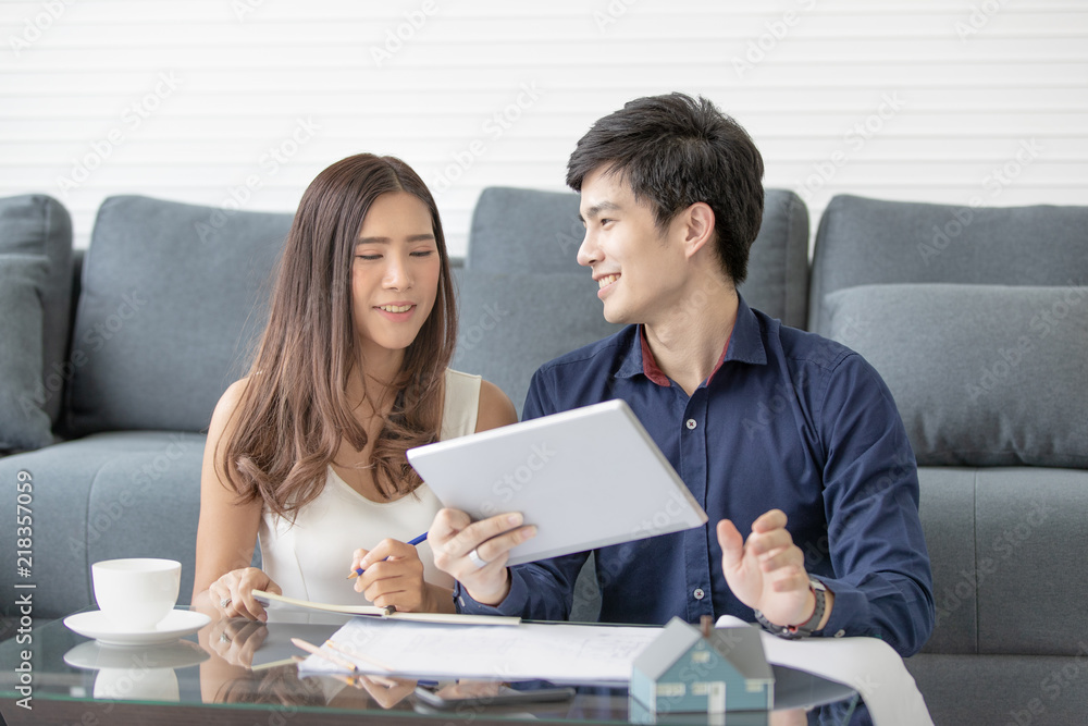 Asian couple smile happily is planning to build his home in the future. Choose from a tablet in hand and plan on table. Asian couple smile happily is planning to build his home in the future. Choose from a tablet in hand and plan on table.
