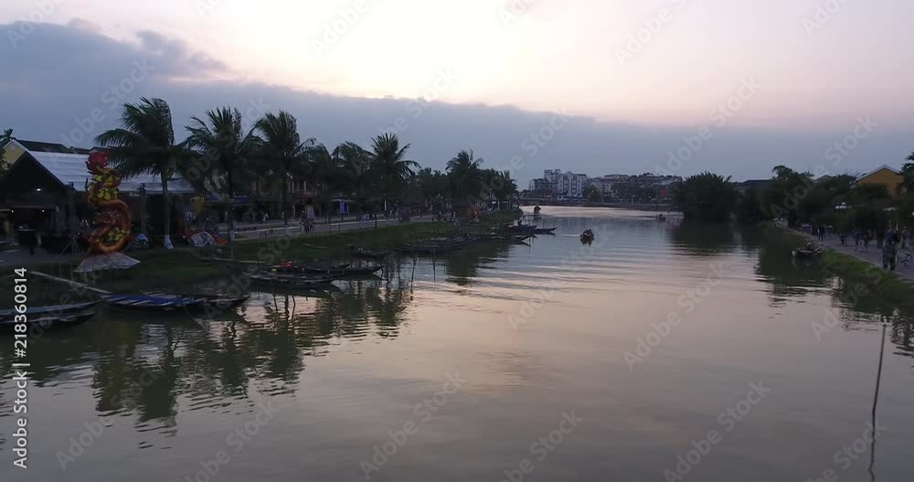 Low shot flying backwards next to the water gliding smoothly beside boats and the shore in Hoi An, Vietnam. Low shot flying backwards next to the water gliding smoothly beside boats and the shore in Hoi An, Vietnam.