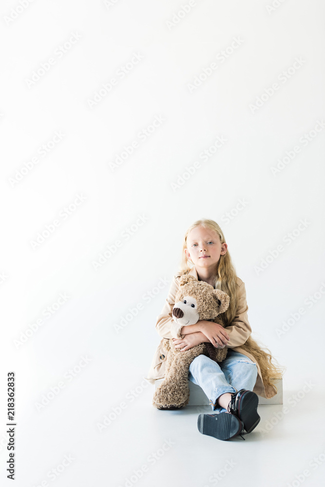 full length view of beautiful little child holding teddy bear and smiling at camera while sitting isolated on white full length view of beautiful little child holding teddy bear and smiling at camera while sitting isolated on white