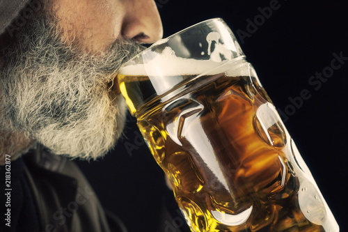 Fotografie A bearded friar (Franciscan religious man) eagerly drinking cold beer from a giant mug