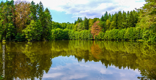 Beautiful trees and sky reflecting on a calm lake surface. Taken in Bavaria, Germany on a sunny fall day.