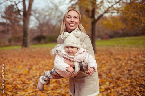 Young mother and little daughter walk in the autumn. Mom and daughter play. Warm winter. Bright autumn.