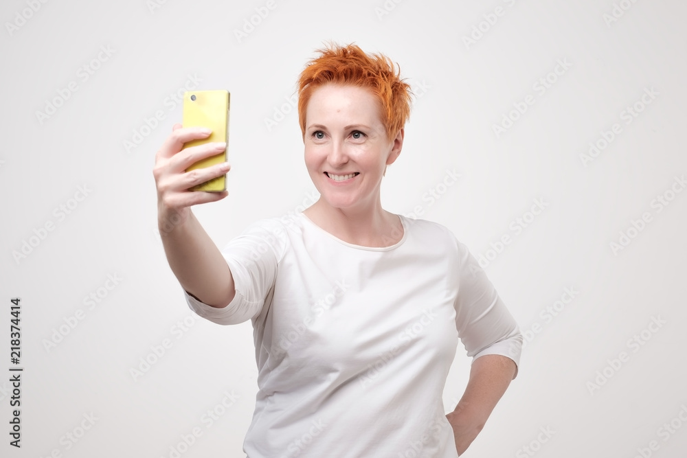 Pretty mature happy woman with red hair making selfie on smartphone Pretty mature happy woman with red hair making selfie on smartphone