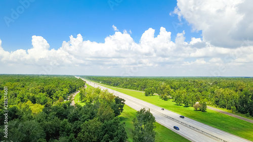 Aerial horizontal view of Interstate 10 highway near rest area with exit and service road. Scenic road surrounded by green oak trees under cloud blue sky in USA. Industry and transportation background