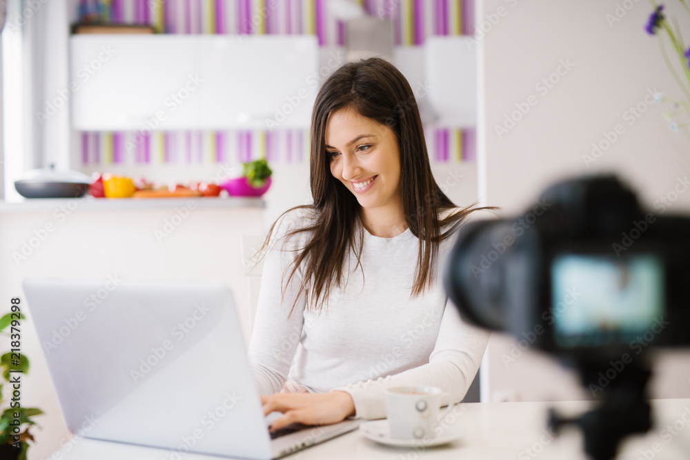 Cheerful beautiful young woman is using her laptop and drinking coffee in front of a camera. Cheerful beautiful young woman is using her laptop and drinking coffee in front of a camera.